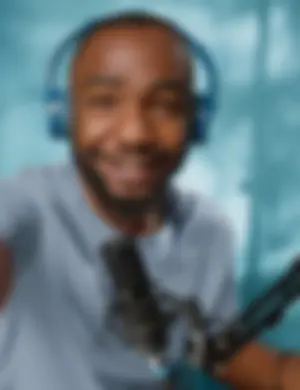 A man in a studio setting wearing headphones and sitting in front of a microphone.