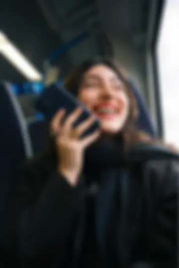 A young woman seated on a subway train, smiling and talking on her phone.